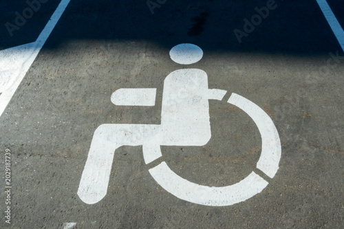 Disabled parking permit symbol on city street pavement in bright daylight. Accessibility icon on ground for urban infrastructure and social inclusion logistics