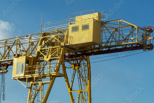 Industrial heavy machinery for lifting and moving cargo at construction site or warehouse. Yellow gantry crane against blue sky background