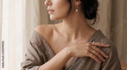 Close-up of woman wearing pearl jewelry and neutral robe in soft window light