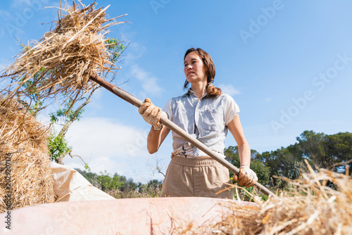 Foto Woman working with pitchfork moving hay on permaculture farm