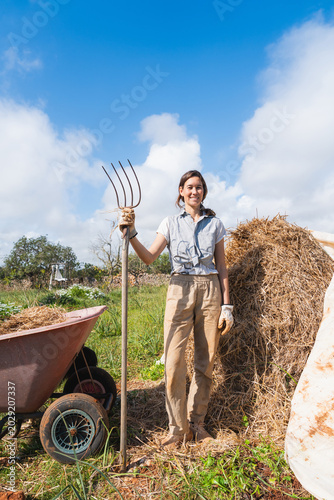Canvas Print Smiling woman working on permaculture farm holding pitchfork