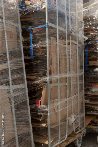 Stacked cartons on rolling metal cages, wrapped in stretch film, barcode tags visible, sterile industrial light, worker absence highlights automated inventory