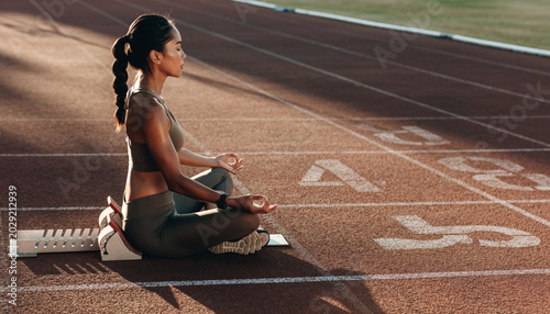 A woman practicing meditation on a running track at sunset.