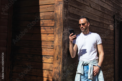 Εκτύπωση καμβά Handsome, casual man using a phone, leaning against a street wall