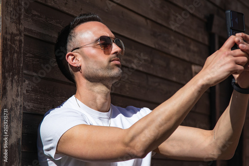 Quadro em tela Handsome, casual man using a phone, leaning against a street wall