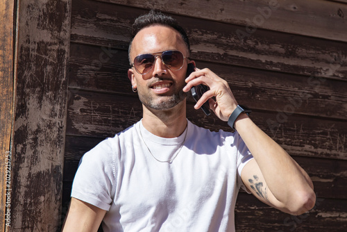Obraz na plátně Handsome, casual man using a phone, leaning against a street wall