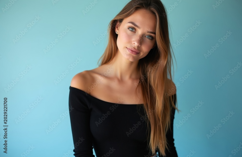 Naklejka premium Young woman with light brown hair wears black off-shoulder top. She poses against soft blue studio background, her direct gaze calm and composed. Attractive person with natural beauty.