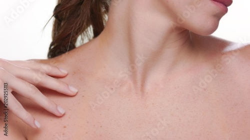 Closeup of Spanish woman with fair skin and freckles strokes her clavicles demonstrating hydrated skin on white background | Body care concept