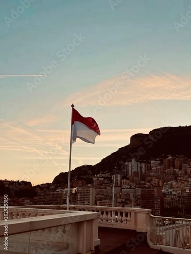 National flag of Monaco waving on a flagpole in Monte Carlo with trees and buildings in background