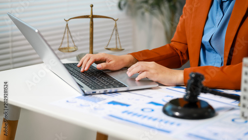 Billede på lærred Businesswoman using laptop at office desk with gavel and scales of justice, legal documents and charts, concept of law firm, compliance, finance, litigation, and legal consulting