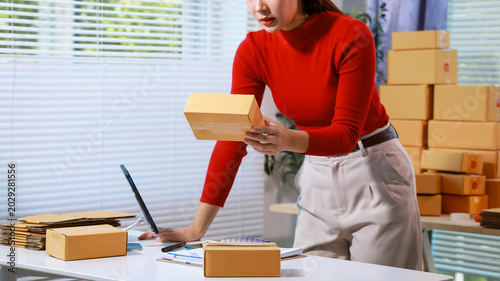 Woman packing and labeling small parcels at home office desk with laptop and boxes, ecommerce order fulfillment, online shop shipping work flow