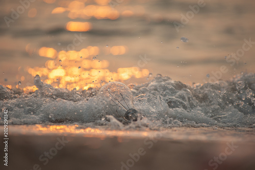 Obraz na płótnie Floating incandescent light bulb washed ashore on the beach in the morning, bathed in the golden yellow light of the setting sun