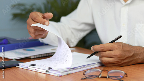 Businessman reviewing financial documents and signing paperwork at office desk. Corporate administration, contract approval, audit process, business agreement, and professional document management 