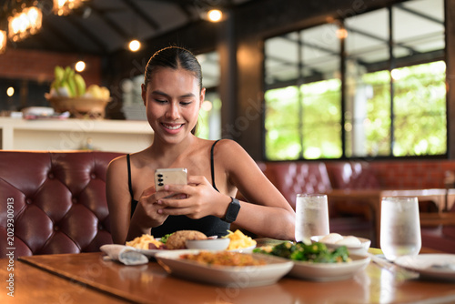 Thai woman smiling and using phone near traditional Thai food