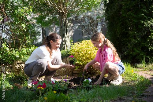 mother and child daughter plant flowers in the garden near the houme on spring day. Kid help mom work in the garden. slow life. enjoy the little things. 