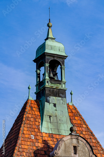 Old church bell tower with green copper roof and tiles. Historic bell tower steeple with weathered green copper patina and orange roof tiles against blue sky. European architecture and travel concept