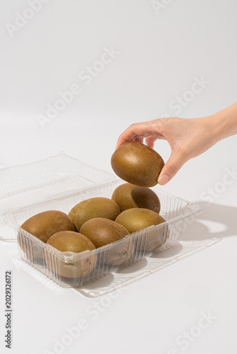 Hand picking a fresh golden kiwi fruit from a transparent plastic packaging container isolated on white background