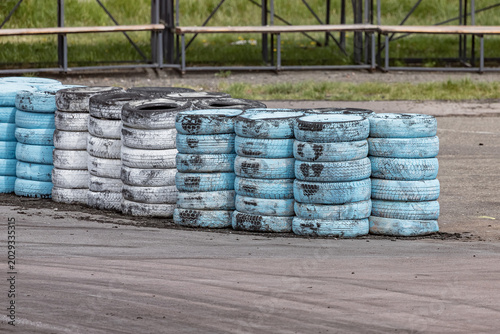 Painted tire barriers at outdoor racing track with asphalt surface. Stacks of blue, white, and black painted tires used as protective barriers at an outdoor motorsport track. 