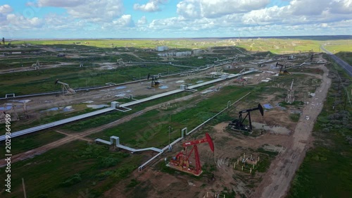 Aerial shot of pumpjack cluster and maintenance pad with exposed soil and equipment crates, service platforms and tool containers near pipeline corridor, subtle oil stains and repair activity