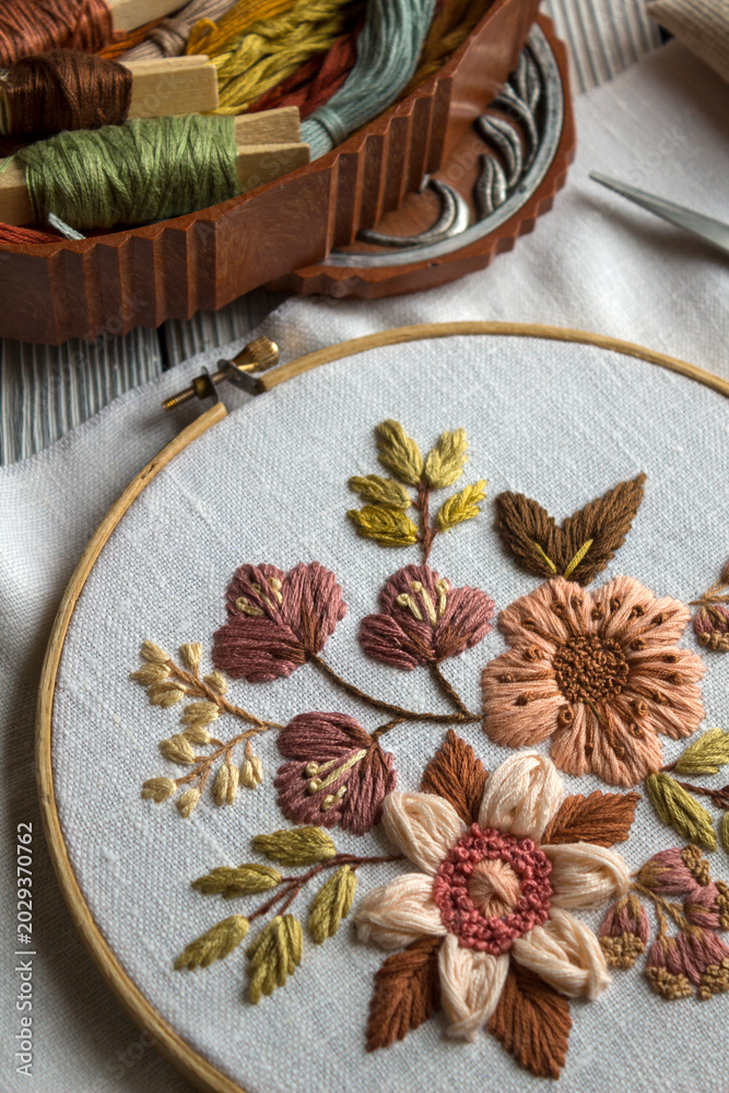 Fototapeta premium Elegant floral embroidery composition in warm brown tones stretched in embroidery hoop with sewing tools nearby. Cozy handmade needlework scene with embroidery supplies and copy space for craft design