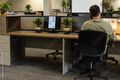 Obraz na plátně Mature man sitting in ergonomic chair at open office holding phone two monitors