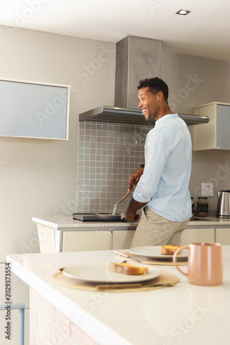 African American man holding spatula cooking on cooktop with frying pan in kitchen, copy space