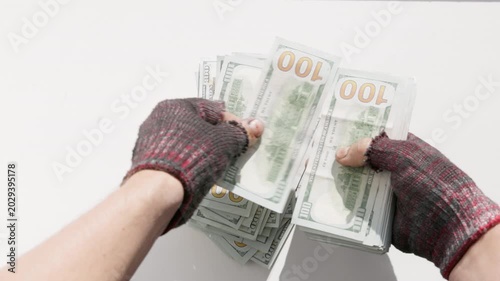 Fingerless gloves hands counting large stack of US dollar fiat money on white table