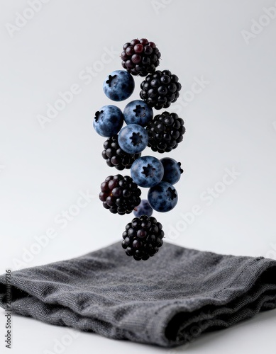Fresh blueberries and blackberries floating in midair above a folded gray cloth on white background. Use: food blog, menu, advertisement.