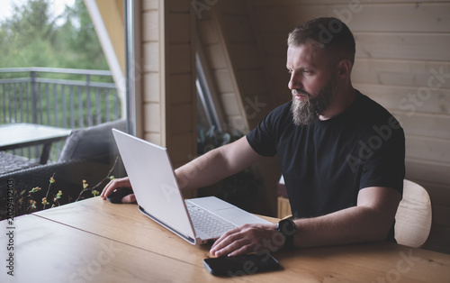 Man with a beard sits at a computer. Freelancer. Open computer on the table. Businessman