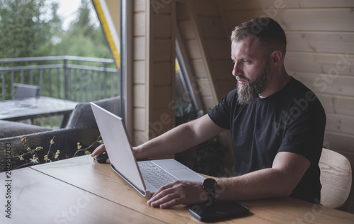 Man with a beard sits at a computer. Freelancer. Open computer on the table. Businessman