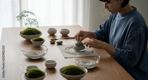 Person creating a zen garden with moss and stones on a wooden table