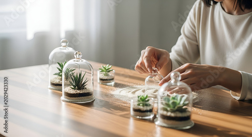 Woman creating mini succulent gardens in glass containers on a wooden table