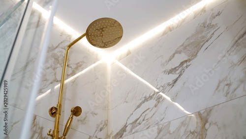 Obraz na plátně Modern gold shower head on white marble wall with glowing led strip lighting