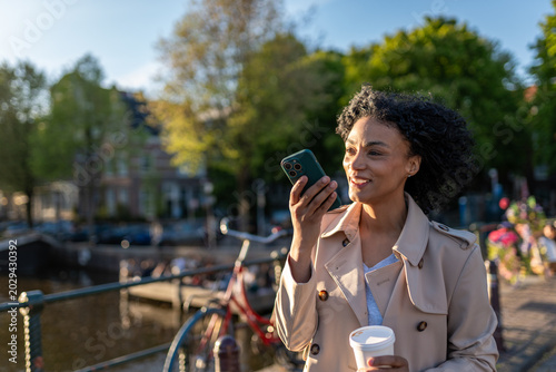 Принти на полотні Happy woman dictating voice message on smartphone while walking on bridge in ams