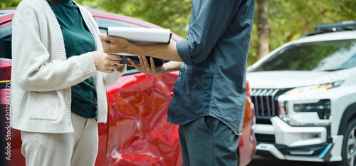 Professional car insurance agent assisting customer with claim documents beside damaged vehicle after collision.