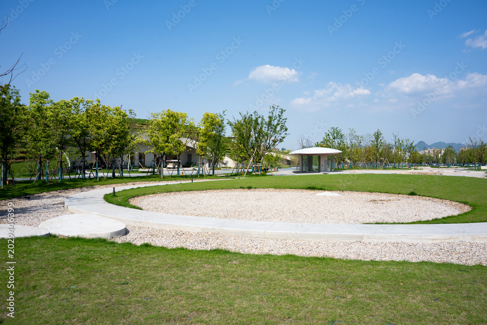 Fototapeta premium Green park landscape with circular path under blue sky and white clouds