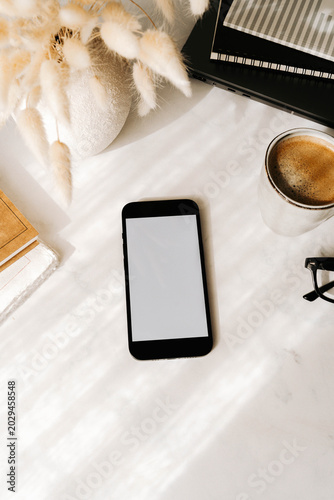 Minimal workspace flat lay with smartphone mock up, coffee, glasses and notebooks on a white desk. Top view