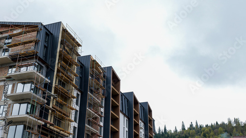 Fényképezés Modern apartment building under construction with scaffolding and forest backdro