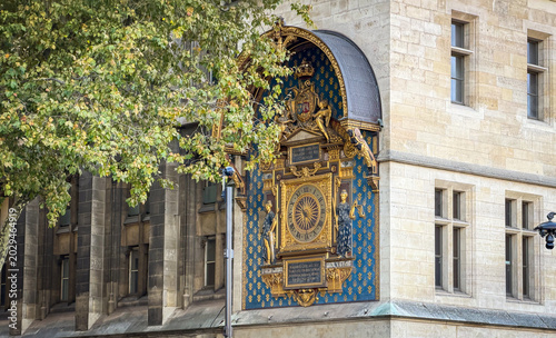 A close-up of the ornate medieval clock (Horloge du Palais de la Cité) set into the stone wall of the Conciergerie building in Paris, France