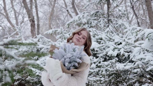 Winter forest serenity, female wearing cozy outerwear standing among snow covered trees, holding festive pine bouquet, experiencing tranquil woodland winter scenery
