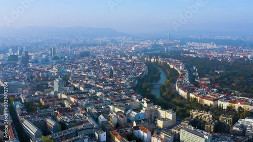 4K aerial wide view of Vienna's dense Habsburg cityscape with the Donaukanal curving toward the Prater and Wienerwald hills shrouded in hazy autumn morning light.