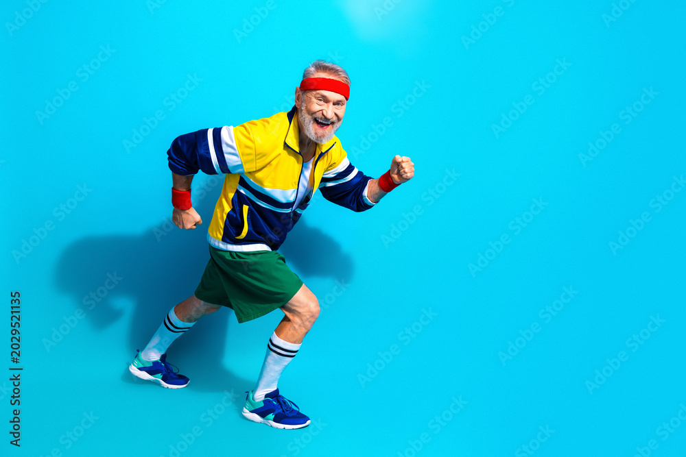 Obraz premium Happy senior man jogging in retro sportswear on blue background — active fitness lifestyle for elderly and mature adults