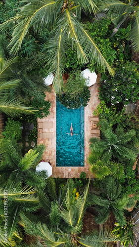 Woman swimming in a refreshing turquoise pool surrounded by lush green palm trees