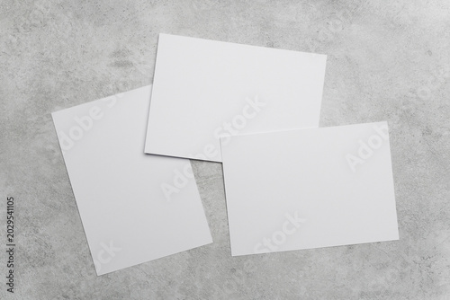 Three blank white sheets of paper with copy space, arranged on a textured gray concrete surface, showcasing a clean and minimalistic design for various creative applications