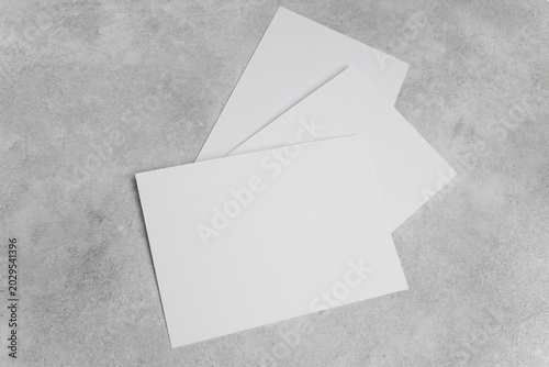 Three blank white cards arranged on a textured gray concrete surface, ideal for design mockups or presentations with ample space for text and graphics