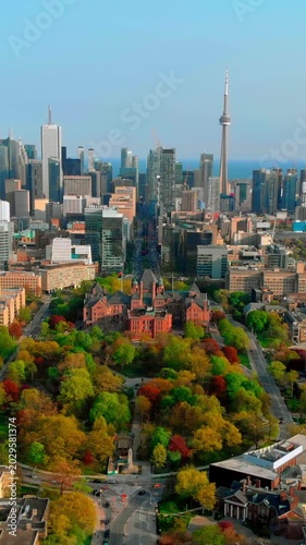 Cinematic toronto aerial at golden hour with warm light bathing redbrick campus and autumn trees, long shadows across park paths, skyline silhouette with cn tower, serene lake horizon, slow drone