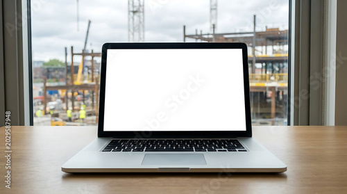 Modern laptop displaying blank screen on wooden desk with construction site in background