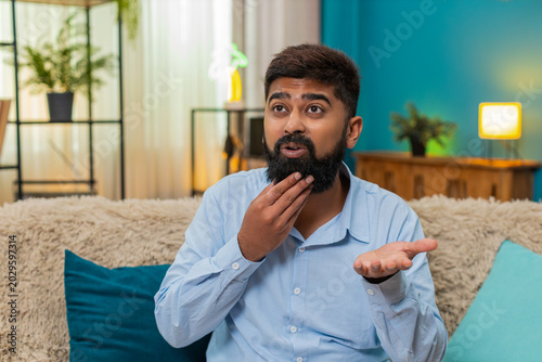 Slika na platnu Indian man at home rolls eyes showing ironic reaction during smartphone chat dismissing odd comment