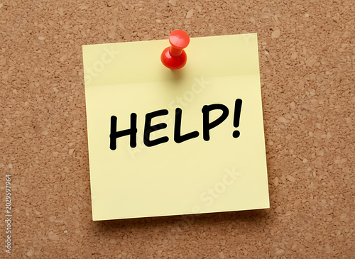 Yellow sticky note with red pushpin saying help on corkboard