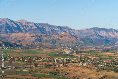 Saranda, Albania - August 26, 2025: High angle view of a wide valley with agricultural fields and villages located at the foot of a high mountain range during sunset